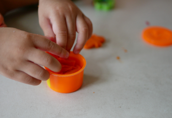 little childs hands playing with orange playdough 350 canva