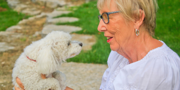 older woman holding her fluffy white poodle and talking happily 